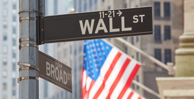 Wall Street sign near Stock Exchange with US flags, financial di Wall Street sign near Stock Exchange with US flags, financial district in New York in a sunny day